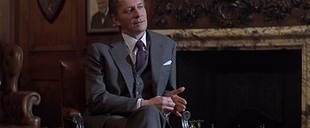 Movie still from “Hanover Street” (1979), directed by Peter Hyams – A man in a suit and tie sitting in front of a fireplace; Medium shot, Over the shoulder angle