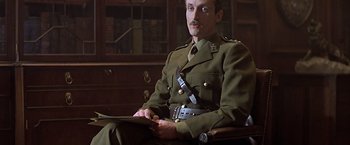 Movie still from “Hanover Street” (1979), directed by Peter Hyams – A man in a military uniform sitting in a chair; Medium shot, Low angle