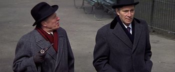 Movie still from “Hanover Street” (1979), directed by Peter Hyams – Two older men in coats and hats standing next to each other; Medium shot, Over the shoulder angle
