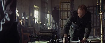 Movie still from “Hanover Street” (1979), directed by Peter Hyams – A man standing in front of an open book case; Medium shot, Low angle