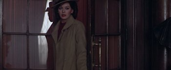 Movie still from “Hanover Street” (1979), directed by Peter Hyams – A woman in a trench coat and hat standing in front of a door; Medium shot, Low angle