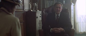 Movie still from “Hanover Street” (1979), directed by Peter Hyams – A man in a suit and tie sitting in a chair; Medium shot, Low angle