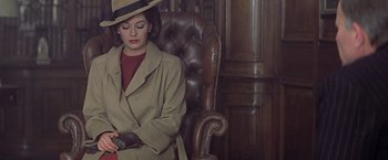 Movie still from “Hanover Street” (1979), directed by Peter Hyams – A woman wearing a hat and a trench coat sitting in a chair; Medium shot, High angle