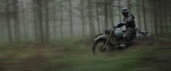 Movie still from “Hanover Street” (1979), directed by Peter Hyams – A person on a motorcycle in the middle of a forest; Wide shot, Low angle