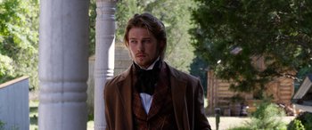 Movie still from “Harriet” (2019), directed by Kasi Lemmons – A man wearing a suit and bow tie standing next to a pole; Medium shot, Over the shoulder angle