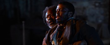 Movie still from “Harriet” (2019), directed by Kasi Lemmons – Two men are standing next to each other in a dark room; Medium shot, Over the shoulder angle