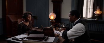 Movie still from “Harriet” (2019), directed by Kasi Lemmons – Two people sitting at a table in front of a lamp; Medium shot, Over the shoulder angle