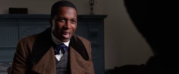Movie still from “Harriet” (2019), directed by Kasi Lemmons – A man wearing a suit and tie with a smile; Close Up shot, Over the shoulder angle