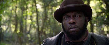 Movie still from “Harriet” (2019), directed by Kasi Lemmons – A person wearing a hat with trees in the background; Close Up shot, Low angle