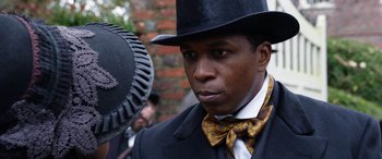 Movie still from “Harriet” (2019), directed by Kasi Lemmons – A man wearing a top hat and a bow tie; Close Up shot, Over the shoulder angle
