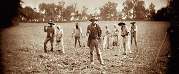 Movie still from “Harriet” (2019), directed by Kasi Lemmons – A group of people in a field with a man holding a stick; Wide shot, High angle