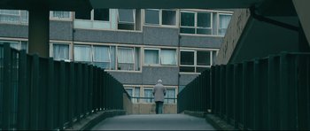 Movie still from “Harry Brown” (2009), directed by Daniel Barber – A person walking down a street near a building; Wide shot, Low angle