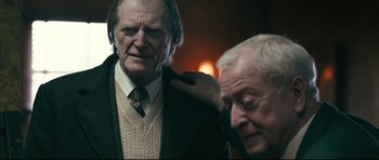 Movie still from “Harry Brown” (2009), directed by Daniel Barber – Two older men standing next to each other in a room; Medium shot, Over the shoulder angle