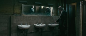 Movie still from “Harry Brown” (2009), directed by Daniel Barber – A woman is standing in front of a mirror in a bathroom; Wide shot, Low angle