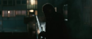 Movie still from “Harry Brown” (2009), directed by Daniel Barber – A man standing in the dark holding a cell phone; Medium shot, Over the shoulder angle