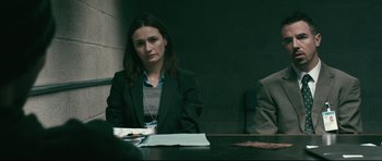 Movie still from “Harry Brown” (2009), directed by Daniel Barber – A woman sitting at a table in a room; Medium shot, Over the shoulder angle