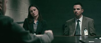 Movie still from “Harry Brown” (2009), directed by Daniel Barber – A woman sitting in front of a man in front of a wall; Medium shot, Over the shoulder angle