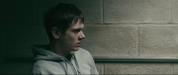 Movie still from “Harry Brown” (2009), directed by Daniel Barber – A young man sitting in front of a brick wall; Close Up shot, Over the shoulder angle
