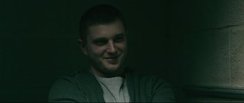 Movie still from “Harry Brown” (2009), directed by Daniel Barber – A young man smiling for the camera in a dark room; Close Up shot, Low angle