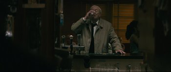Movie still from “Harry Brown” (2009), directed by Daniel Barber – An older man drinking a glass of beer; Medium shot, Over the shoulder angle