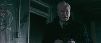 Movie still from “Harry Brown” (2009), directed by Daniel Barber – An older man in a black coat holding a camera; Medium shot, Over the shoulder angle