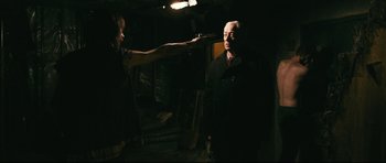 Movie still from “Harry Brown” (2009), directed by Daniel Barber – A woman pointing a gun at an older man in a dark room; Medium shot, Over the shoulder angle