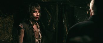 Movie still from “Harry Brown” (2009), directed by Daniel Barber – A man with long dark hair standing in the dark; Medium shot, Over the shoulder angle