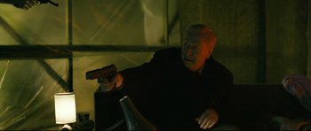 Movie still from “Harry Brown” (2009), directed by Daniel Barber – An older man holding a gun while sitting in a dark room; Medium shot, High angle