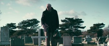 Movie still from “Harry Brown” (2009), directed by Daniel Barber – An older man in a black coat is standing in a cemetery; Medium shot, Low angle