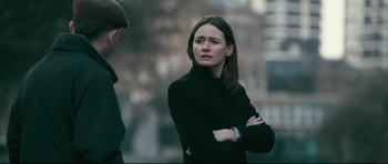 Movie still from “Harry Brown” (2009), directed by Daniel Barber – A woman in a black coat is standing with her arms crossed; Medium shot, Over the shoulder angle