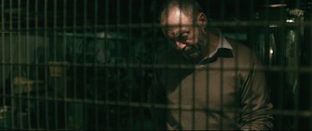 Movie still from “Harry Brown” (2009), directed by Daniel Barber – A man with a beard is standing behind a fence; Close Up shot, Low angle