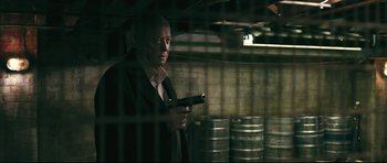 Movie still from “Harry Brown” (2009), directed by Daniel Barber – A man holding a gun while standing next to a wall; Medium shot, Low angle