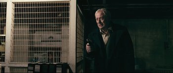 Movie still from “Harry Brown” (2009), directed by Daniel Barber – An older man holding a cell phone while standing next to a building; Medium shot, Low angle