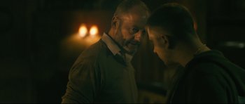 Movie still from “Harry Brown” (2009), directed by Daniel Barber – A man standing next to another man in a dark room; Close Up shot, Over the shoulder angle