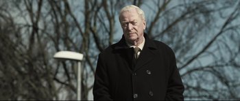 Movie still from “Harry Brown” (2009), directed by Daniel Barber – An older man wearing a black coat and a tie; Medium shot, Over the shoulder angle
