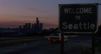 Movie still from “Harry and the Hendersons” (1987), directed by William Dear – A car driving down a street next to a welcome to seattle sign; Extreme Wide shot, Low angle