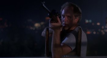 Movie still from “Harry and the Hendersons” (1987), directed by William Dear – A man sitting in a chair holding a rifle; Medium shot, Low angle