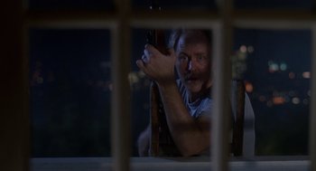 Movie still from “Harry and the Hendersons” (1987), directed by William Dear – A man holding a gun looking through a window at night; Medium shot, Low angle