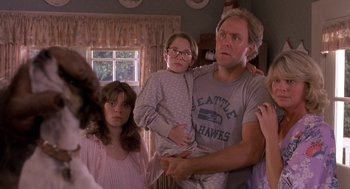 Movie still from “Harry and the Hendersons” (1987), directed by William Dear – A man and two girls in a living room; Medium shot, Over the shoulder angle
