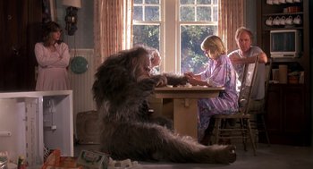 Movie still from “Harry and the Hendersons” (1987), directed by William Dear – A group of people sitting around a table playing a game; Wide shot, High angle