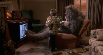 Movie still from “Harry and the Hendersons” (1987), directed by William Dear – A young boy is watching tv with an animal; Medium shot, Over the shoulder angle