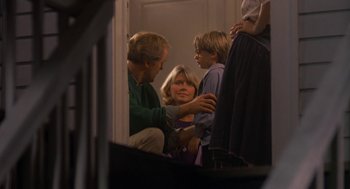 Movie still from “Harry and the Hendersons” (1987), directed by William Dear – A woman and two children are sitting on the stairs; Medium shot, Over the shoulder angle