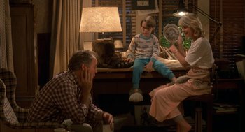 Movie still from “Harry and the Hendersons” (1987), directed by William Dear – A group of people sitting around a living room together; Wide shot, High angle