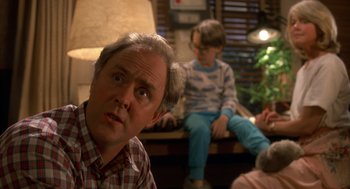 Movie still from “Harry and the Hendersons” (1987), directed by William Dear – A person sitting on a couch; Close Up shot, Over the shoulder angle