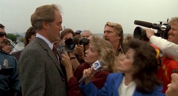 Movie still from “Harry and the Hendersons” (1987), directed by William Dear – A group of people gathered around a man talking to a camera; Medium shot, Over the shoulder angle