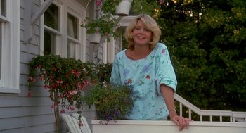 Movie still from “Harry and the Hendersons” (1987), directed by William Dear – A woman standing on a porch with a potted plant; Medium shot, Low angle