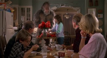 Movie still from “Harry and the Hendersons” (1987), directed by William Dear – A group of people sitting around a table with flowers; Wide shot, Over the shoulder angle