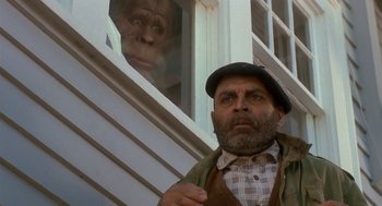 Movie still from “Harry and the Hendersons” (1987), directed by William Dear – A man standing next to a window with a monkey behind him; Close Up shot, Low angle