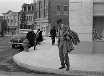 Movie still from “Harvey” (1950), directed by Henry Koster – An old black and white photo of a man standing on the side of the street; Wide shot, Over the shoulder angle