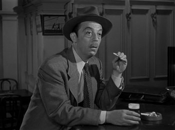 Movie still from “Harvey” (1950), directed by Henry Koster – A man sitting at a table with a cigarette in his mouth; Medium shot, Low angle